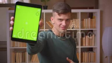在平板电脑上打开应用程序的年轻男学生的肖像显示了它的绿色彩屏，并在图书馆竖起大拇指。